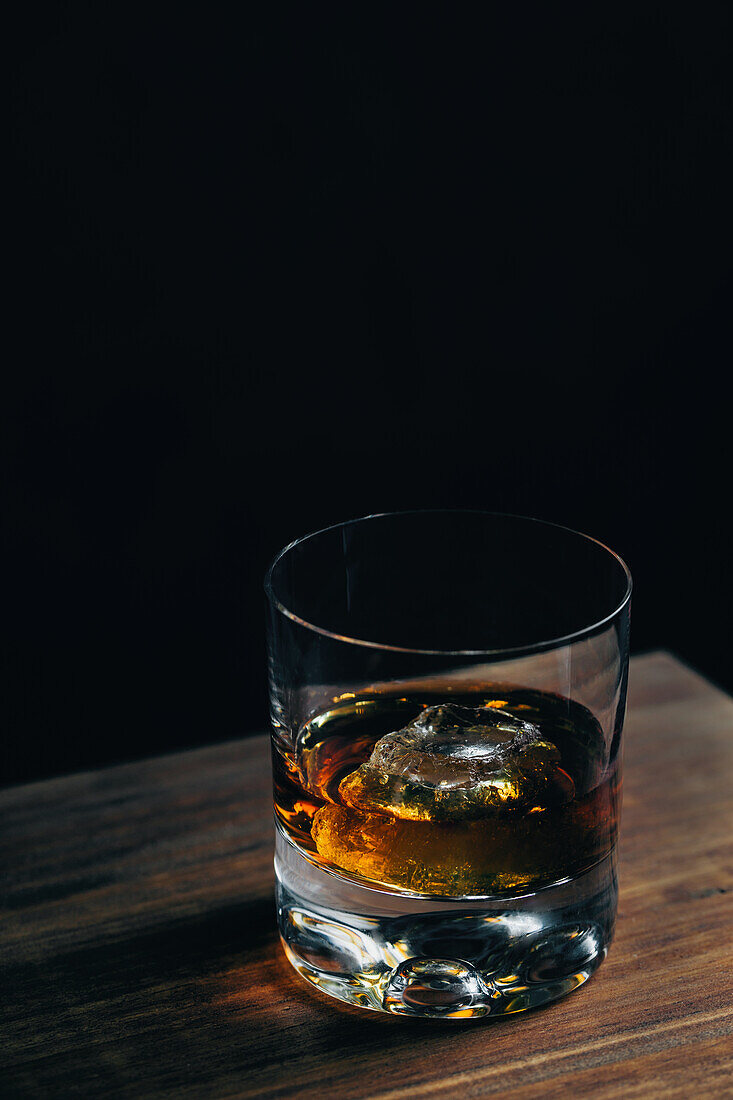 Von oben Glasbecher mit kaltem Whiskey und Eiswürfel auf Holztisch in dunklem Raum platziert