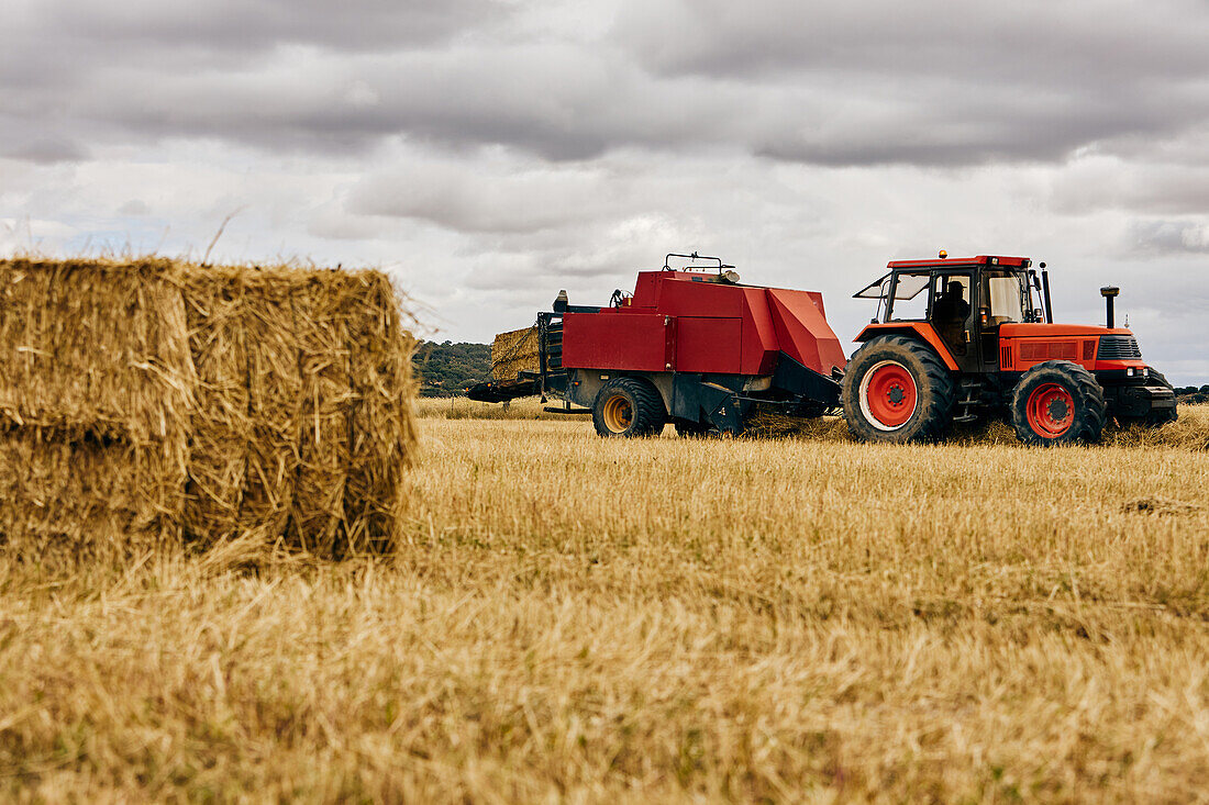 Dried hay roll and modern tractor placed on agricultural field in mountainous area in summer