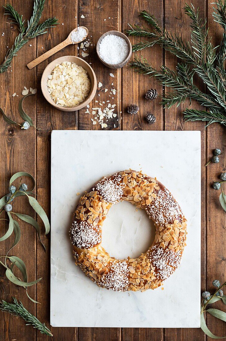 Overhead view of tasty three kings cake decorated with almond petals and coconut flakes among Eucalyptus and fir sprigs