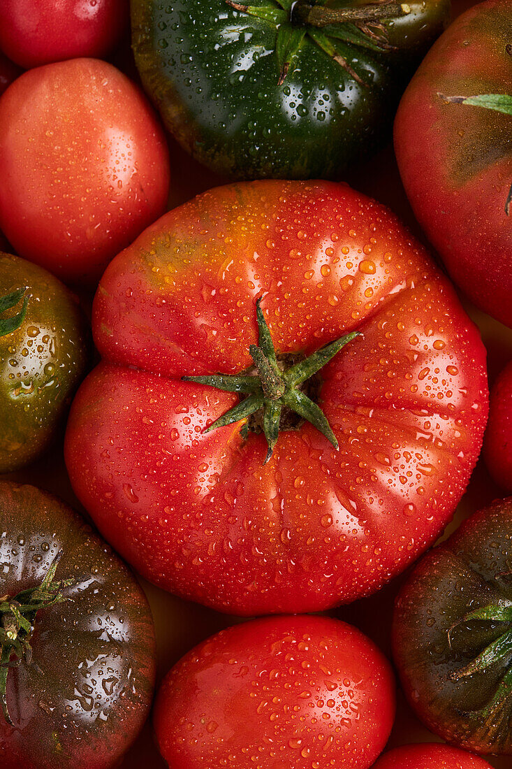 From above of appetizing fresh ripe tomatoes with drops of water near branch with green leaves