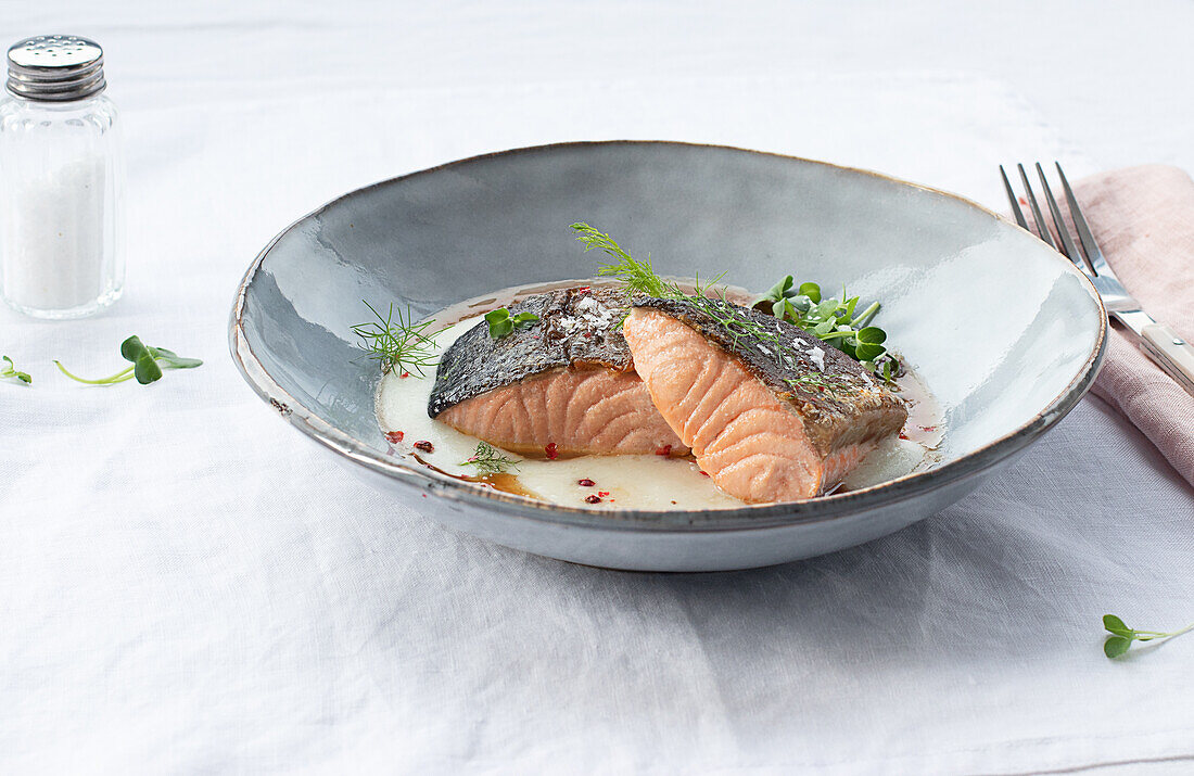 Von oben köstlicher Lachs mit Kartoffelpüree mit grünen Blättern und Gewürzen auf Keramikteller auf Tisch