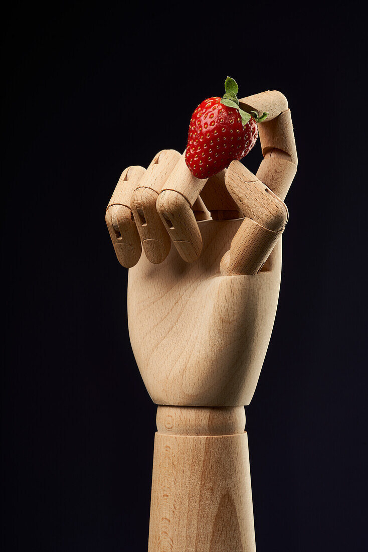 Reife süße Erdbeere in hölzerner Hand auf schwarzem Hintergrund im Studio für gesundes Essen Konzept