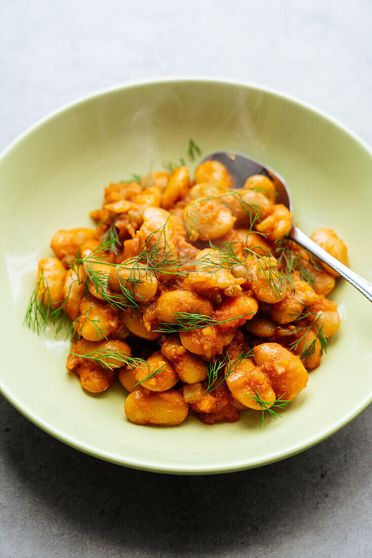 From above of delicious traditional Greek giant naked beans in tomato sauce served in plate on gray background in kitchen