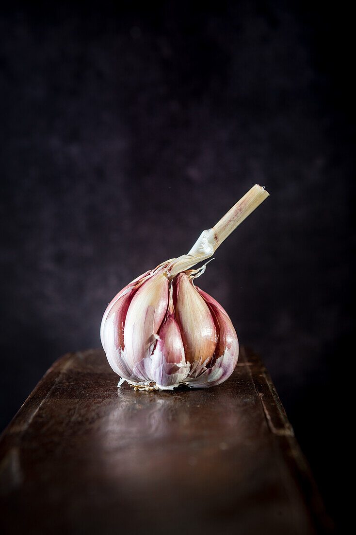 Whole head of fresh garlic placed on shabby wooden table in rustic kitchen with dark background