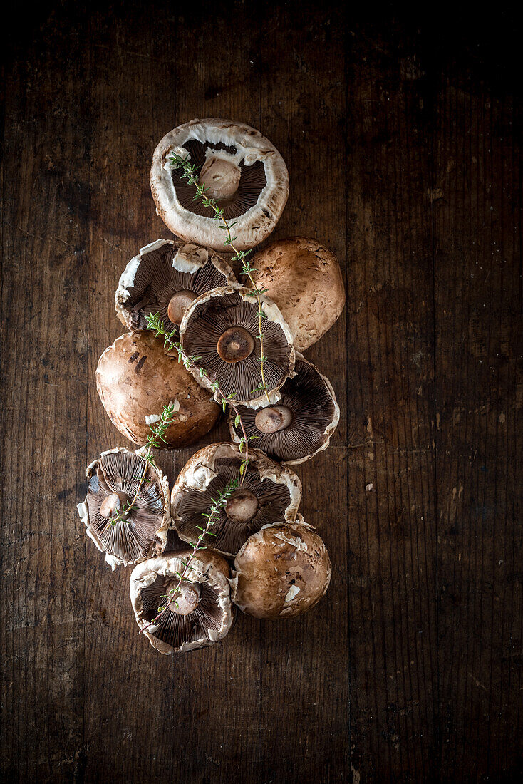 Top view of fresh raw champignons and sprigs of herbs placed on rustic wooden table