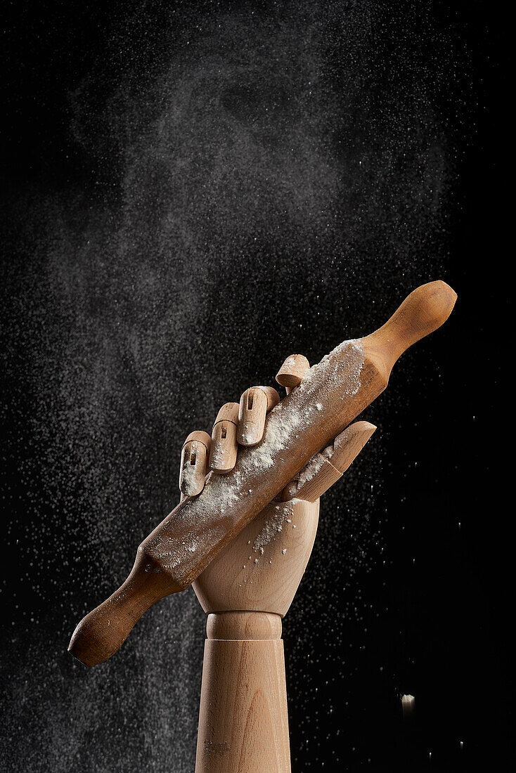 Rolling pin in flour in wooden hand on black background in studio showing concept of culinary