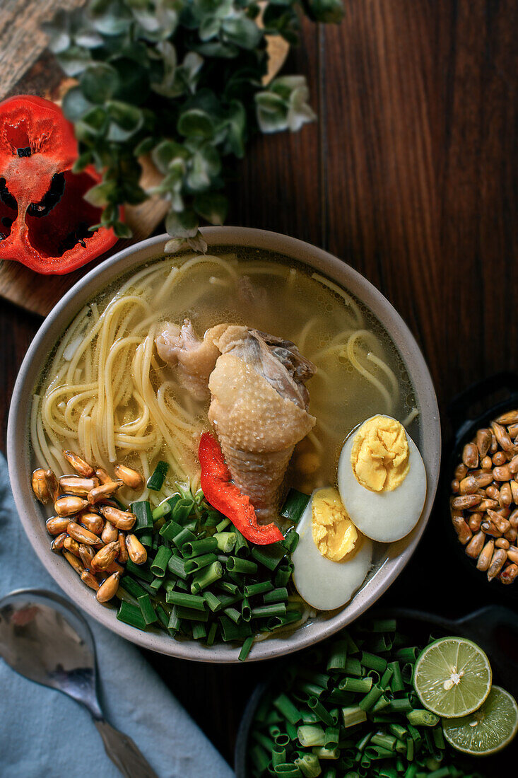 Appetitliche frische Hühnerbrühe mit verschiedenen Zutaten in einer Schüssel auf einem Küchentisch von oben