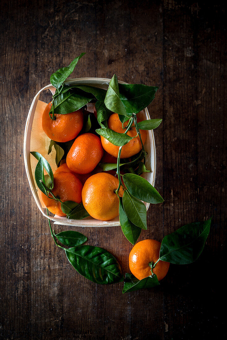 Overhead view of bright fresh tangerines with green foliage in rectangular shaped container on wooden table