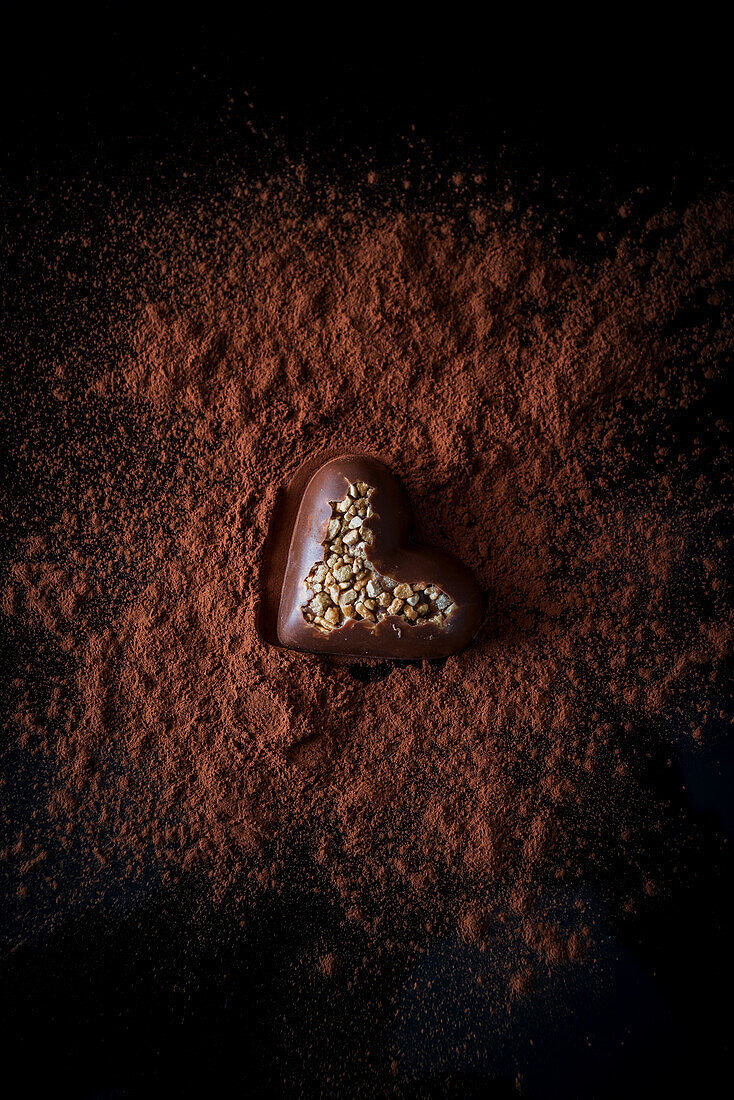 Herzförmige Schokoladenpralinen mit Nüssen auf einem Tisch mit Kakaopulver auf schwarzem Hintergrund von oben