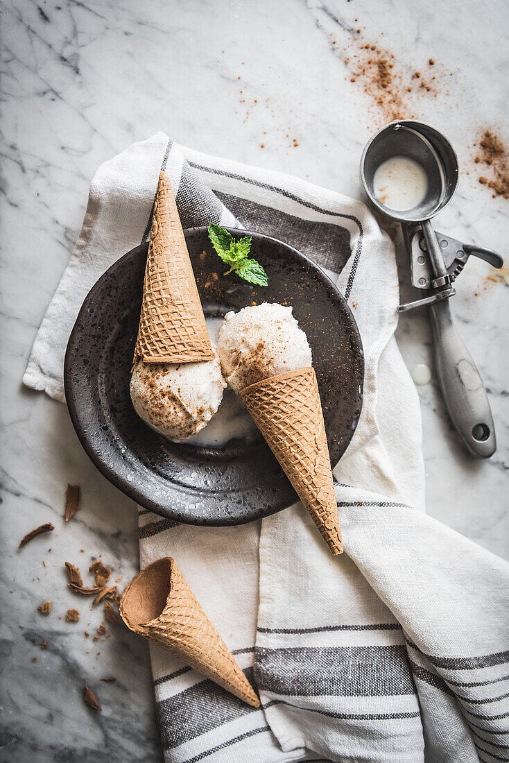 From above of waffle cones with meringue milk gelato scoops and fresh mint leaves with cinnamon powder on top