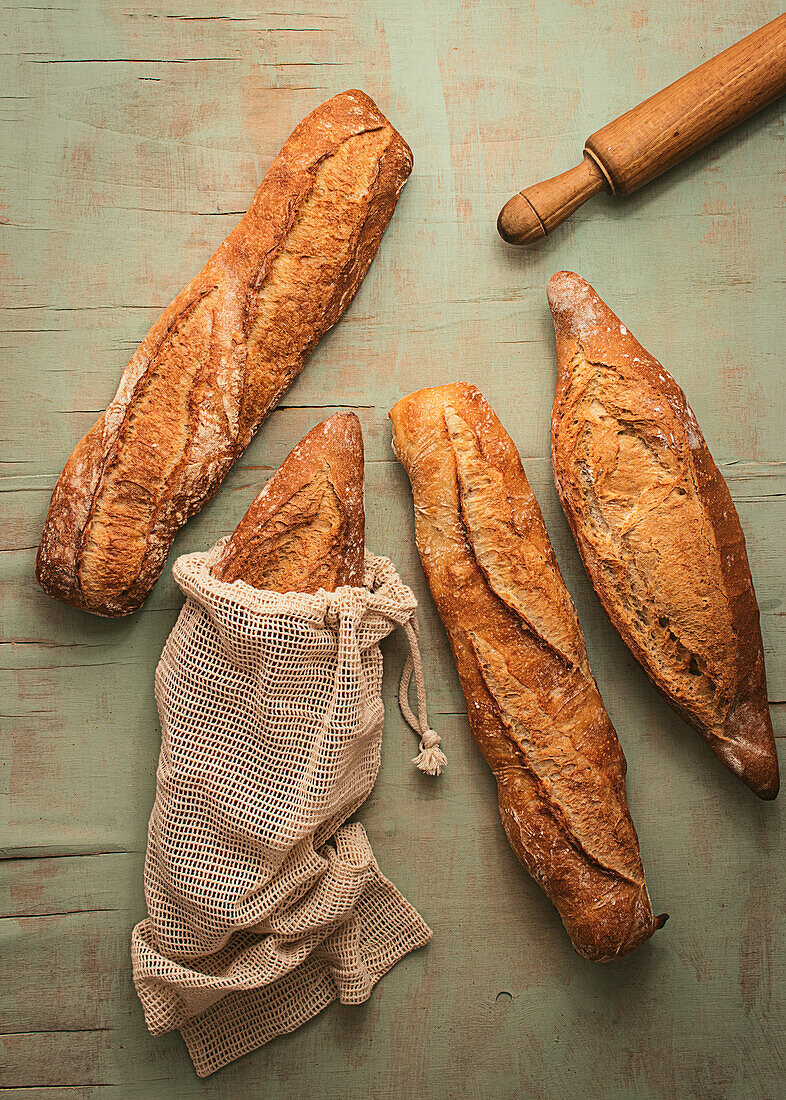 Top view composition of delicious crispy artisan sourdough bread loaves packed in burlap bags on green background