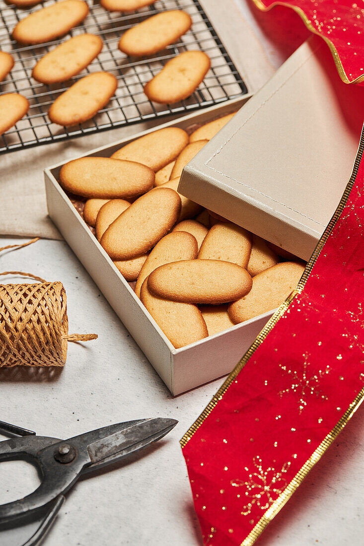 From above of tasty Christmas biscuits placed on metal baking net and box on table with assorted wrapping supplies
