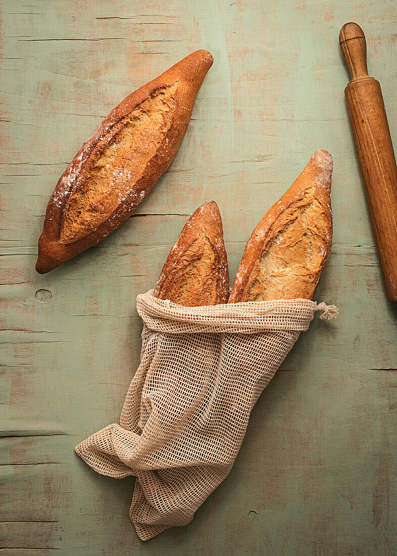 Komposition aus köstlichem, knusprigem Sauerteigbrot, verpackt in Leinensäcken, auf grünem Hintergrund