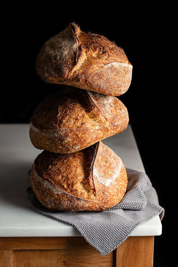 Leckeres Sauerteigbrot mit brauner Kruste auf Marmortisch vor schwarzem Hintergrund