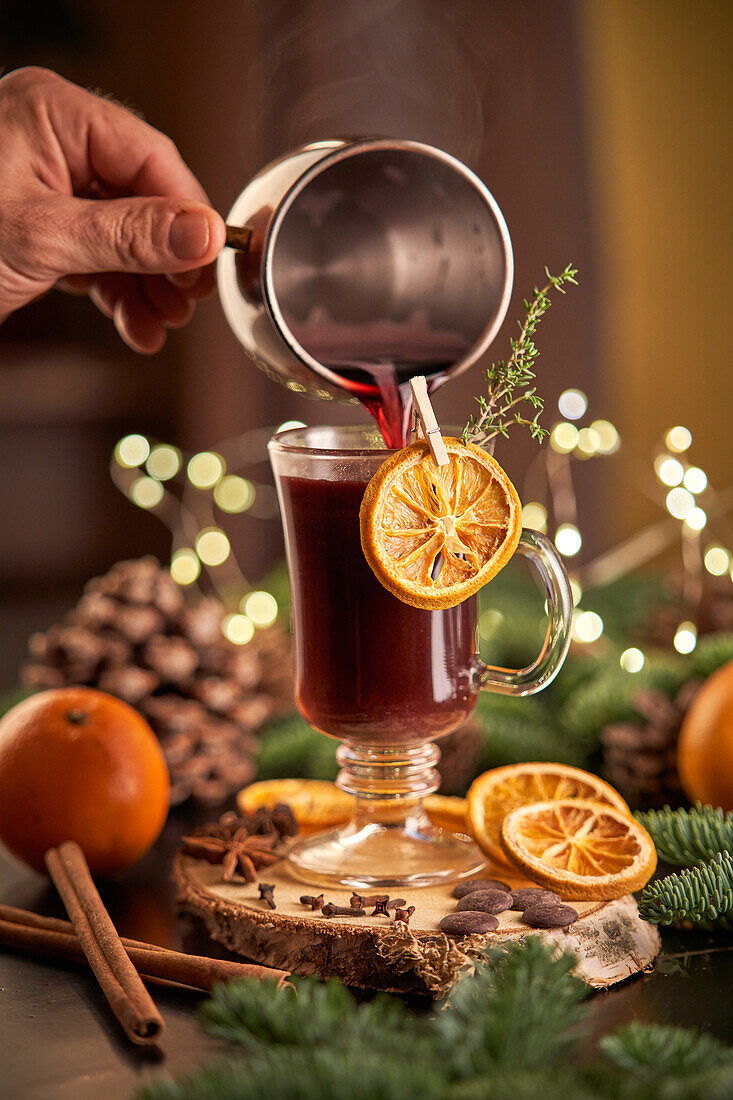 Anonyme Erntehelferin serviert Glühwein oder Weihnachtspunsch in einem Glasbecher mit getrockneten Orangenscheiben