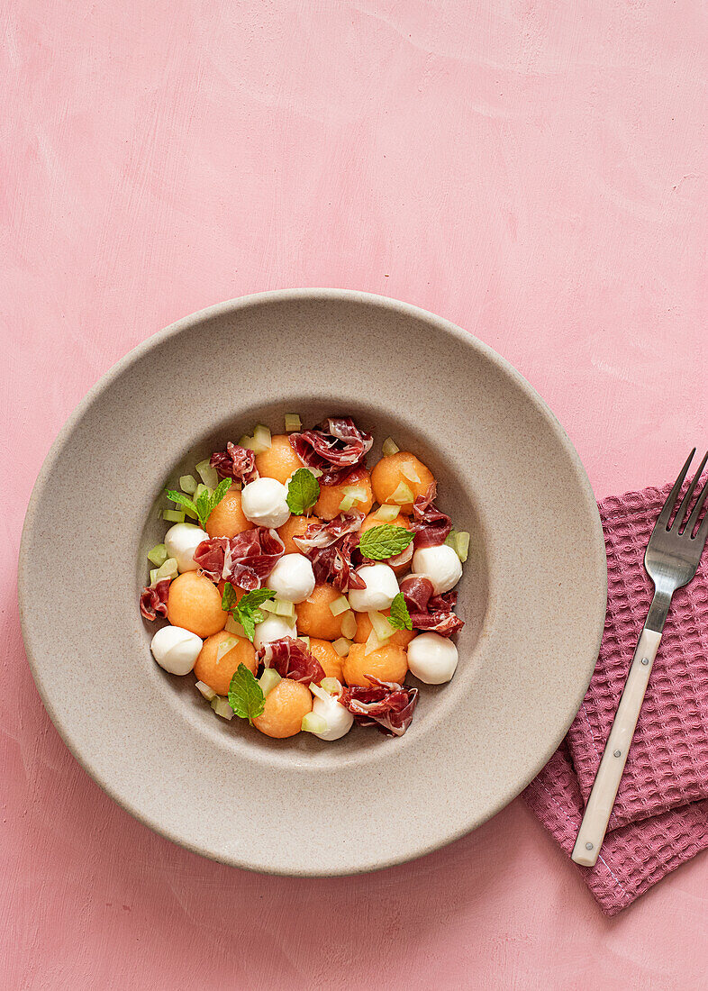 Von oben exotischer Melonen-, Mozzarella- und Prosciutto-Salat auf rosafarbenem Hintergrund