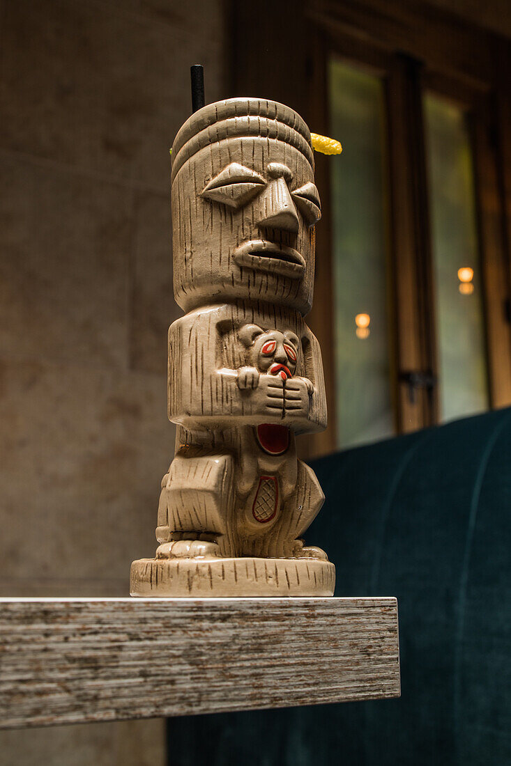 Traditional sculptural tiki cup of alcohol drink with straw placed on wooden table