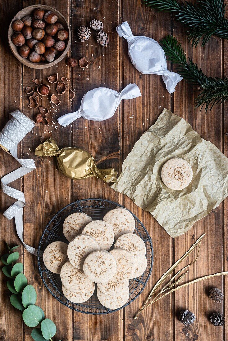 Draufsicht auf eine Reihe süßer, runder Butterkekse mit Haselnüssen, die mit Geschenkpapier und Bändern auf einem Holztisch arrangiert sind