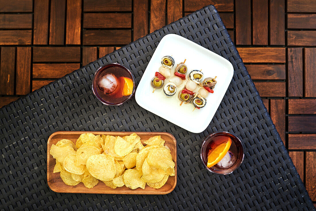 From above of glass with cold old fashioned cocktail with ice and orange slice served on table with appetizers