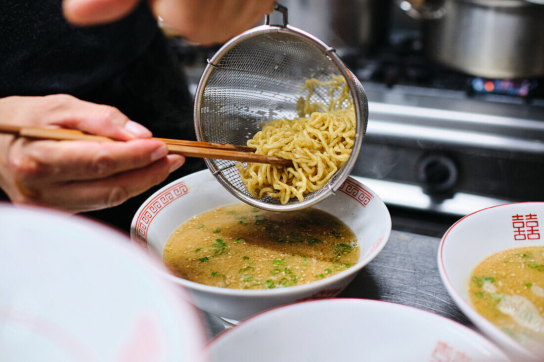 Stock photo of unrecognized chef in japanese restaurant serving noddles soup.