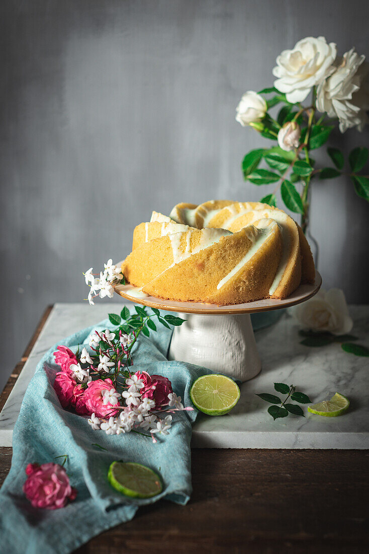 Tasty lime sponge cake served on white plate near flowers and lime slices