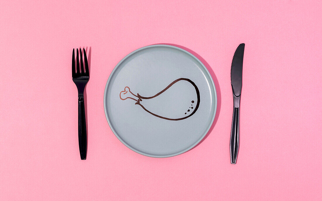 Draufsicht auf eine schwarze Plastikgabel und ein schwarzes Plastikmesser, die auf einem rosa Tisch auf einem grauen Teller mit einer gemalten Cartoon-Hühnerkeule liegen