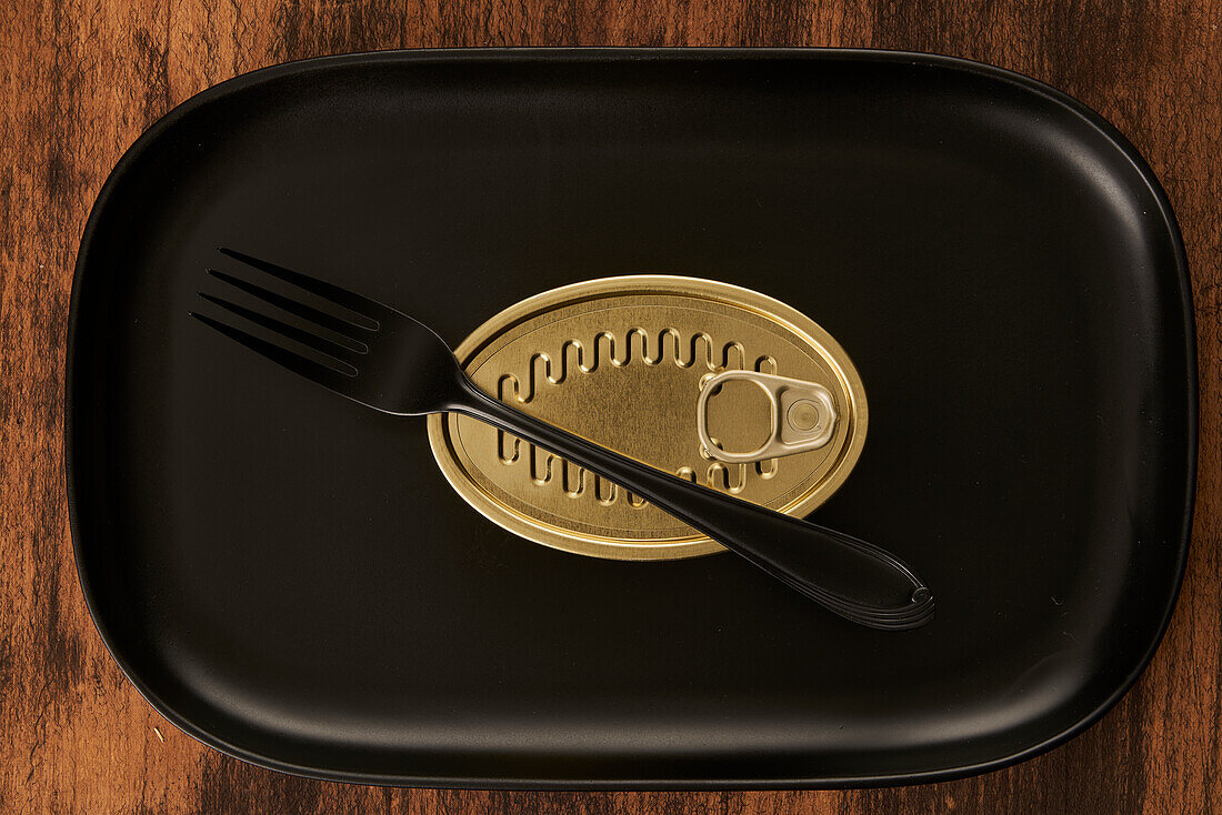 Top view of black fork placed near sealed canned food on rectangular black tray