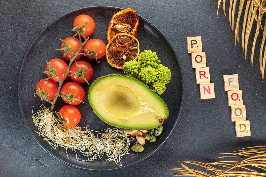 Top view of decorative inscription near plate with fresh half of avocado and bundle of cherry tomatoes near red orange slices