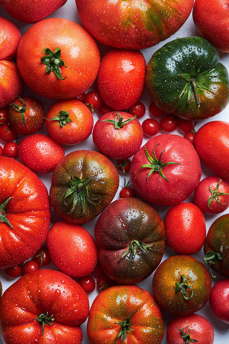 From above of appetizing fresh ripe tomatoes with drops of water near branch with green leaves