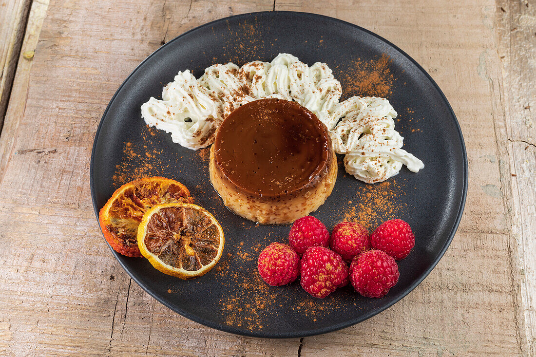From above of tasty flan with whipped cream and red orange slices with cinnamon powder on ceramic plate