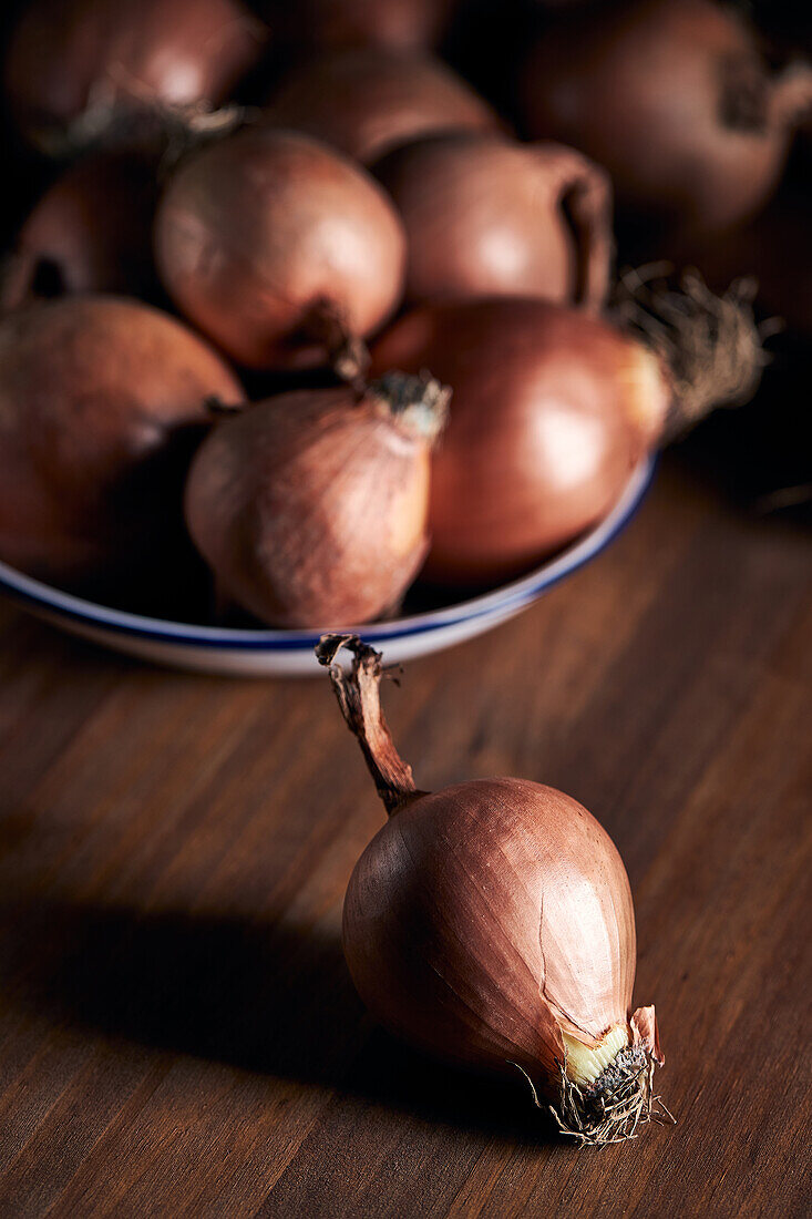 Hoher Winkel eines Bündels frischer ungeschälter Zwiebeln auf einem Teller auf einem Holztisch