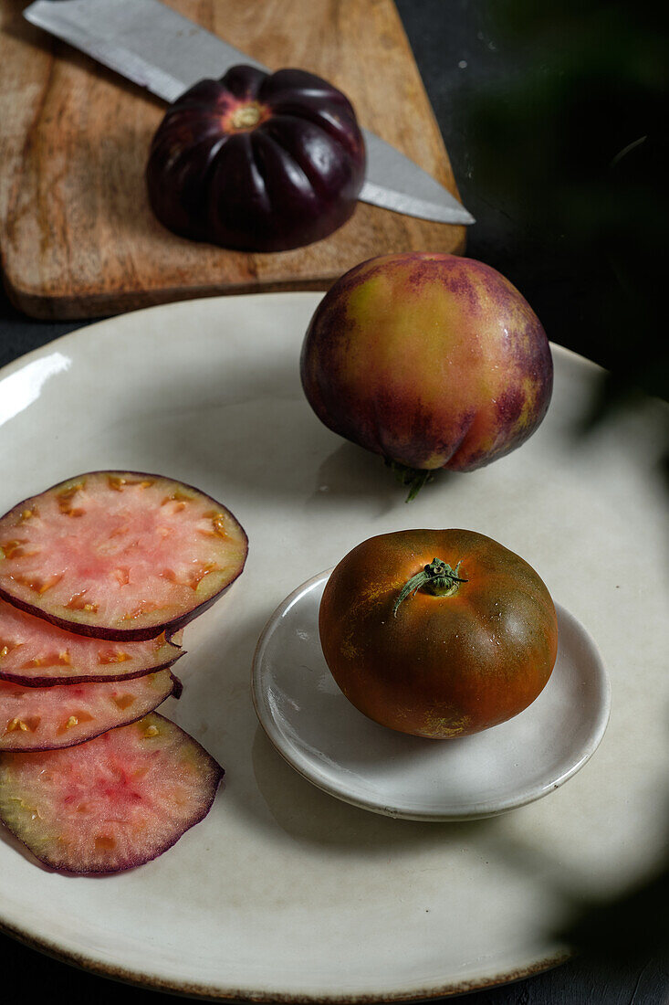 From above fresh whole and sliced black tomatoes on table during healthy meal preparation