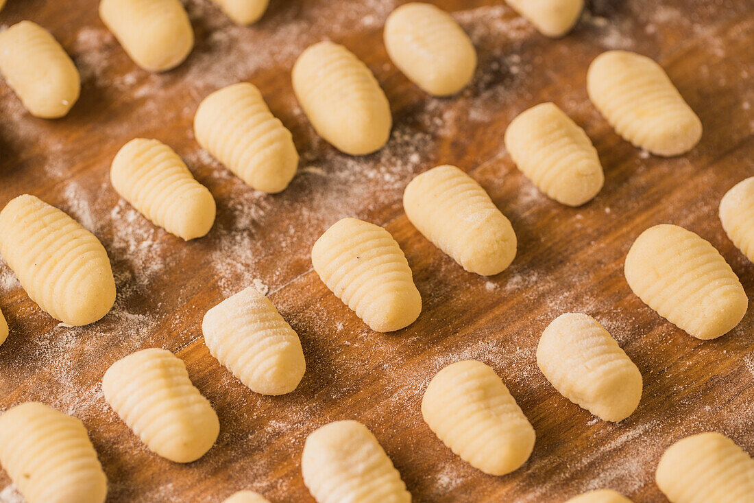 Blick von oben auf ungekochte Gnocchi, die während der Zubereitung des Mittagessens zu Hause in geordneten Reihen auf einem Holztisch liegen