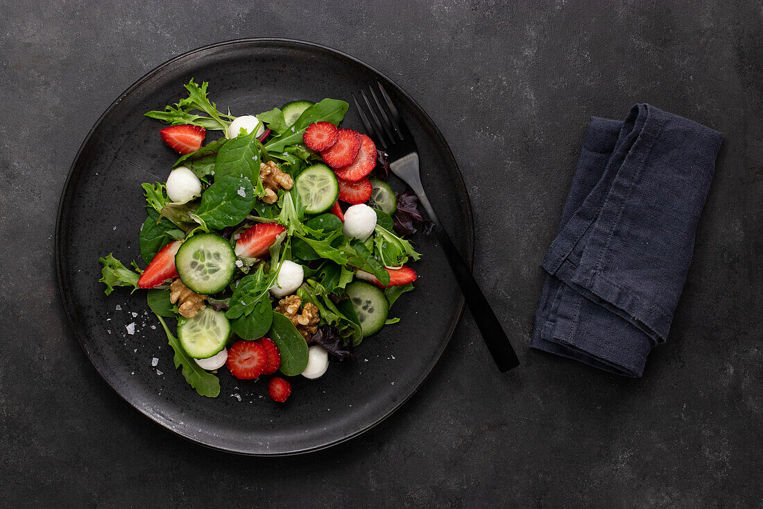 Dish with a summer salad of strawberries and cucumber on a dark table