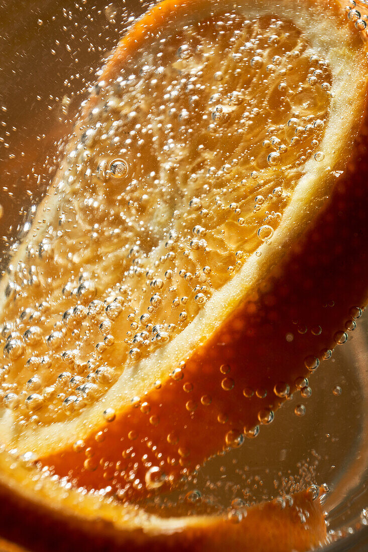 Nahaufnahme eines Gin-Tonic-Cocktails mit einer frischen Orangenscheibe, die im Glas blubbert