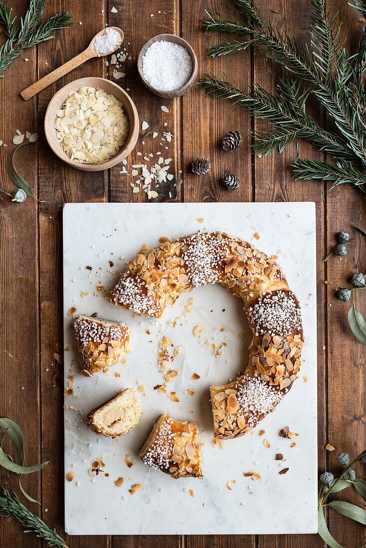 Overhead view of tasty three kings cake decorated with almond petals and coconut flakes among Eucalyptus and fir sprigs