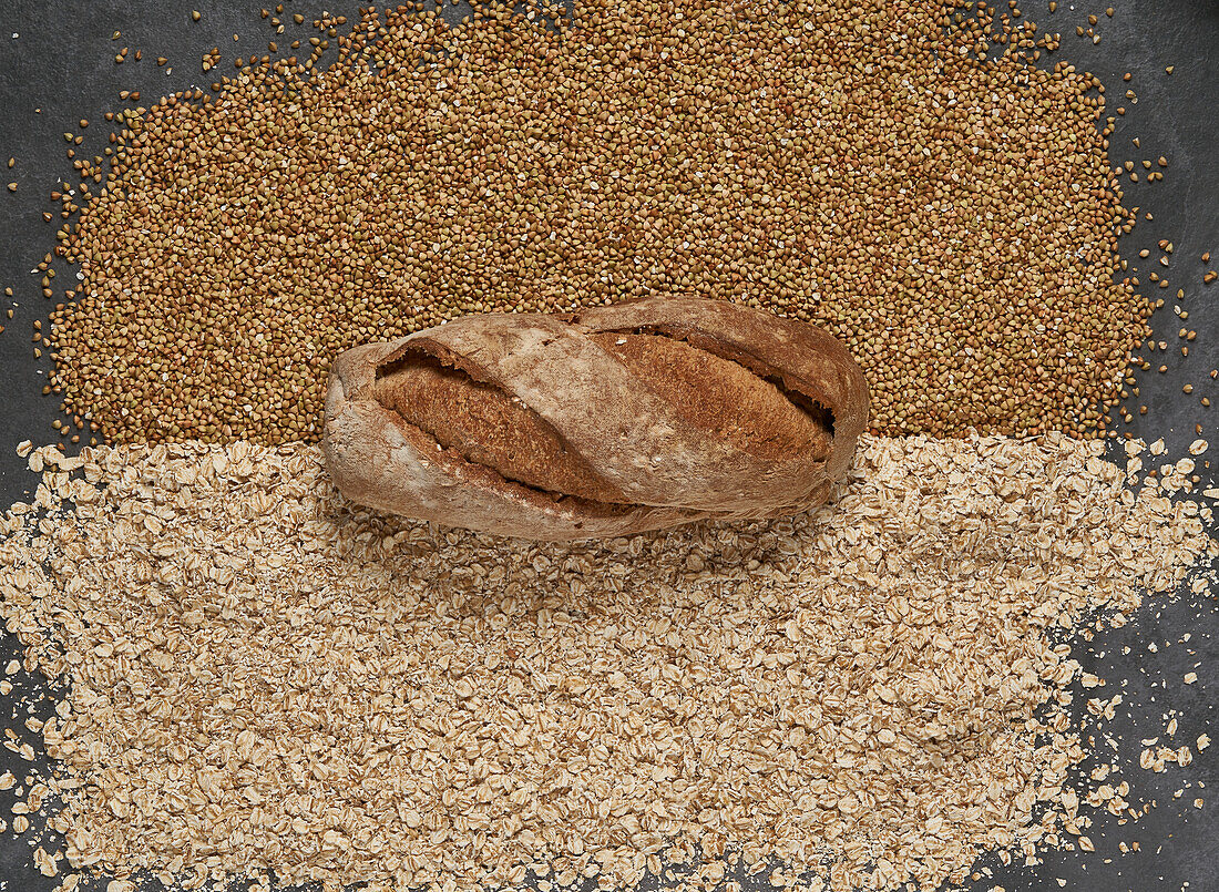 Draufsicht Vollbild von frischem gesundem braunem gebackenem Brot auf rohen Buchweizen und Haferkörnern in hellem Raum