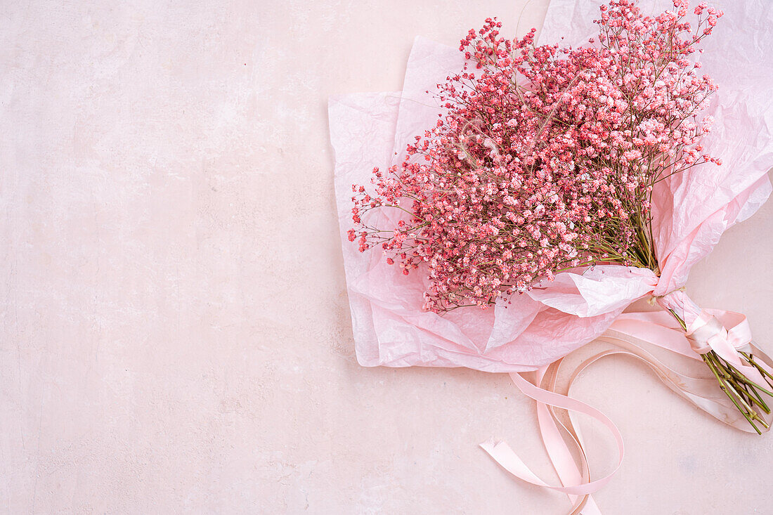 Von oben: Blumenstrauß aus kleinen zarten Gypsophila-Blüten mit grünen Stängeln in einer Papierverpackung auf rosa Hintergrund in einem hellen Raum