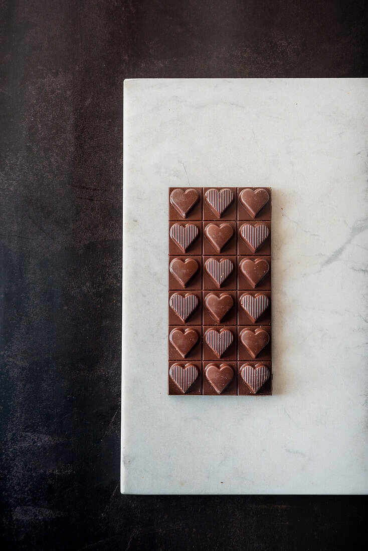 Draufsicht auf köstliche Schokoladenbonbons mit Nüssen in Herzform auf Marmortablett auf Tischhintergrund