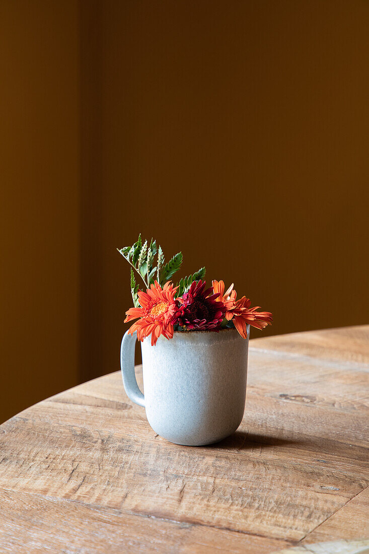 Keramiktasse mit frischen, blühenden Blumen auf einem Holztisch in einem Restaurant bei Tageslicht
