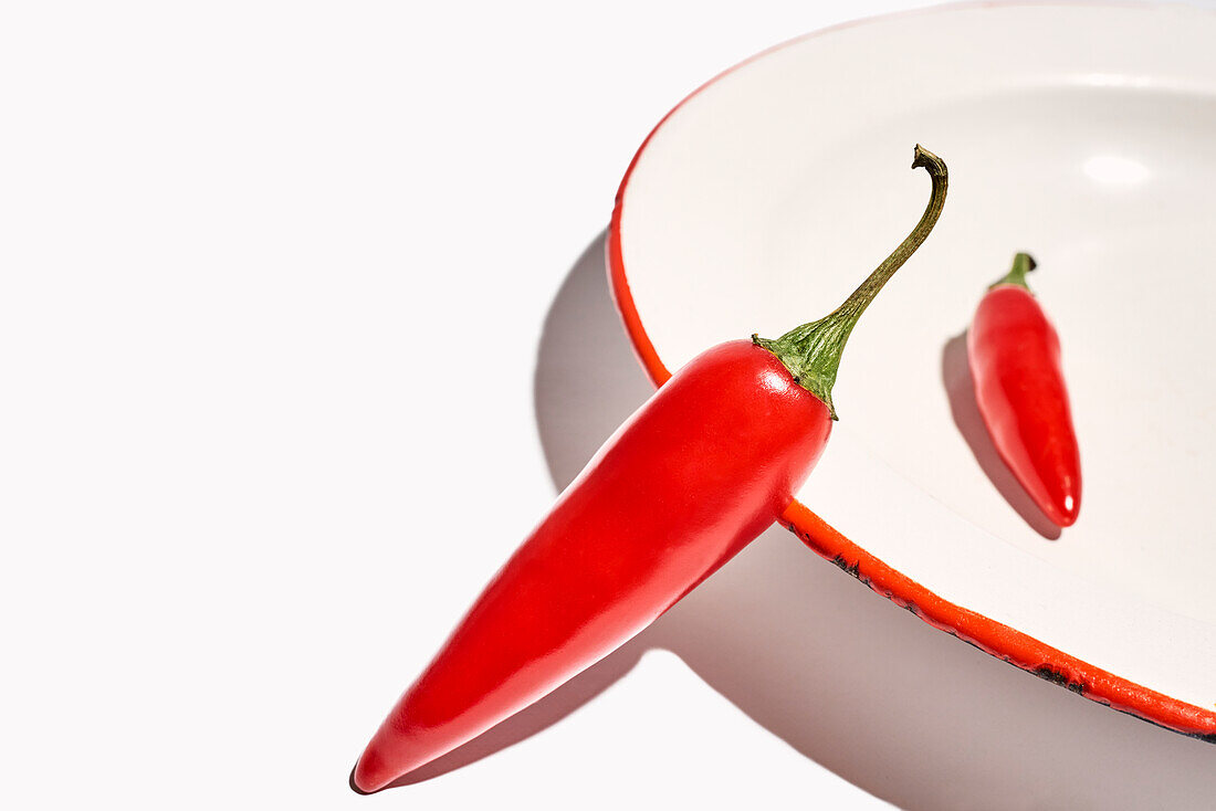 Top view composition of bowl with hot peppers with green stem placed on white background