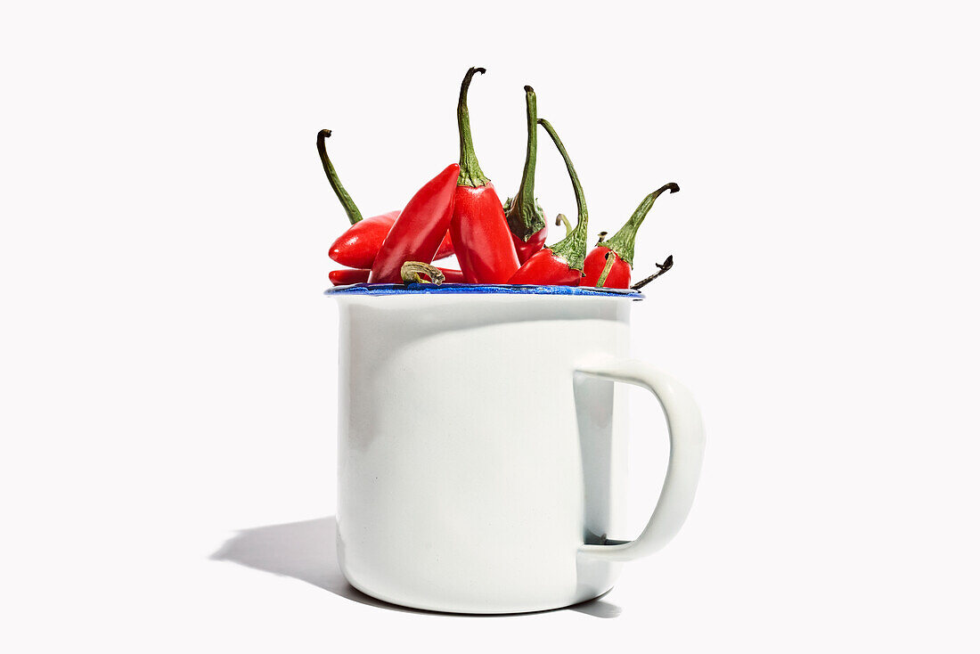 Big ceramic mug full of ripe fresh exotic pepper placed on white background