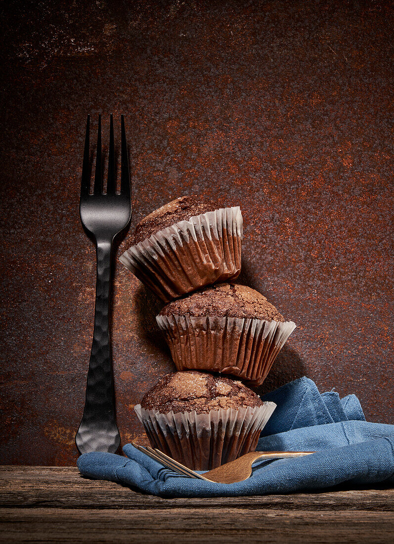 Stapel leckerer süßer Schokoladenmuffins übereinander auf einem Holztisch mit blauem Handtuch und Gabeln