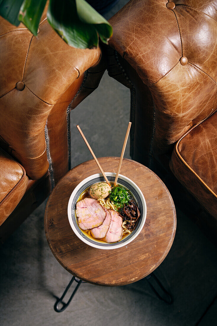 Top view of delicious traditional ramen soup in bowl with chopsticks served on round table