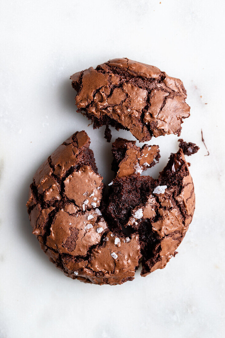 Top view of homemade baked broken sweet chocolate brownie cookie with cracks and crumbs placed on white background in light kitchen