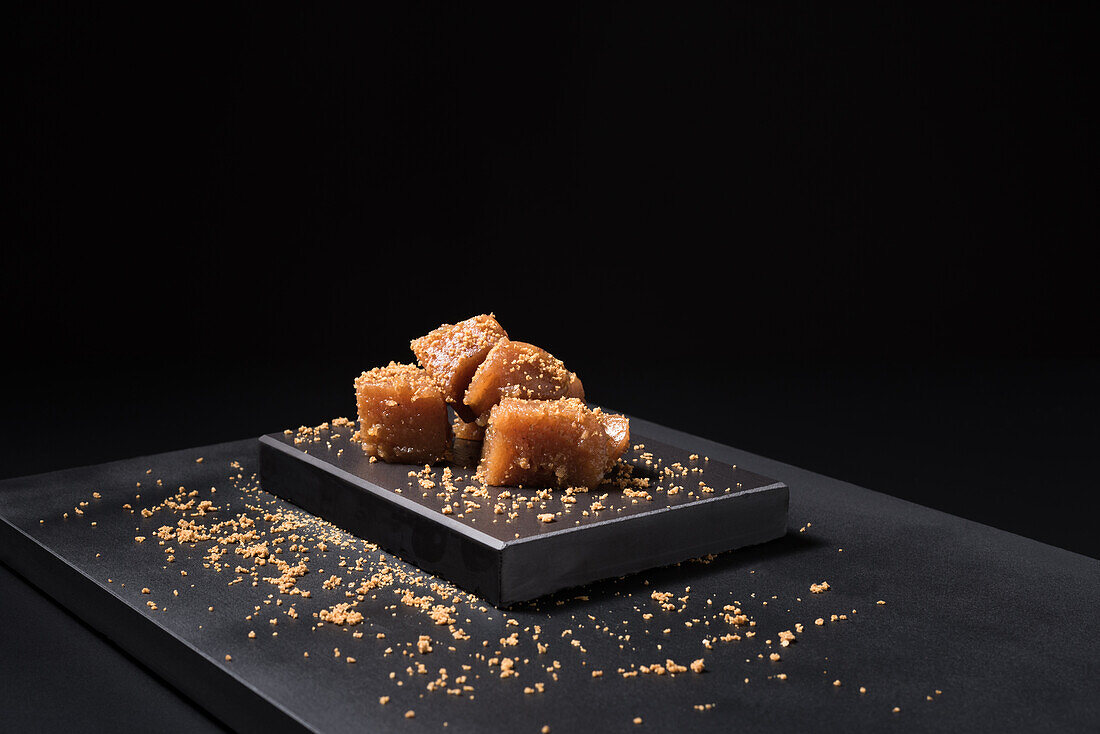 Gourmet quince jelly paste in ceramic plate sprinkled with sesame seeds on black background