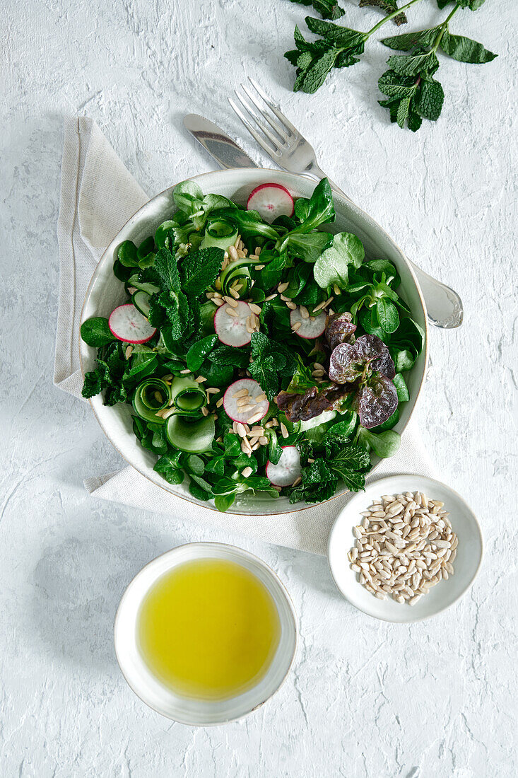 Top view of fresh healthy vegetable salad in bowl served on table with olive oil and sunflower seeds