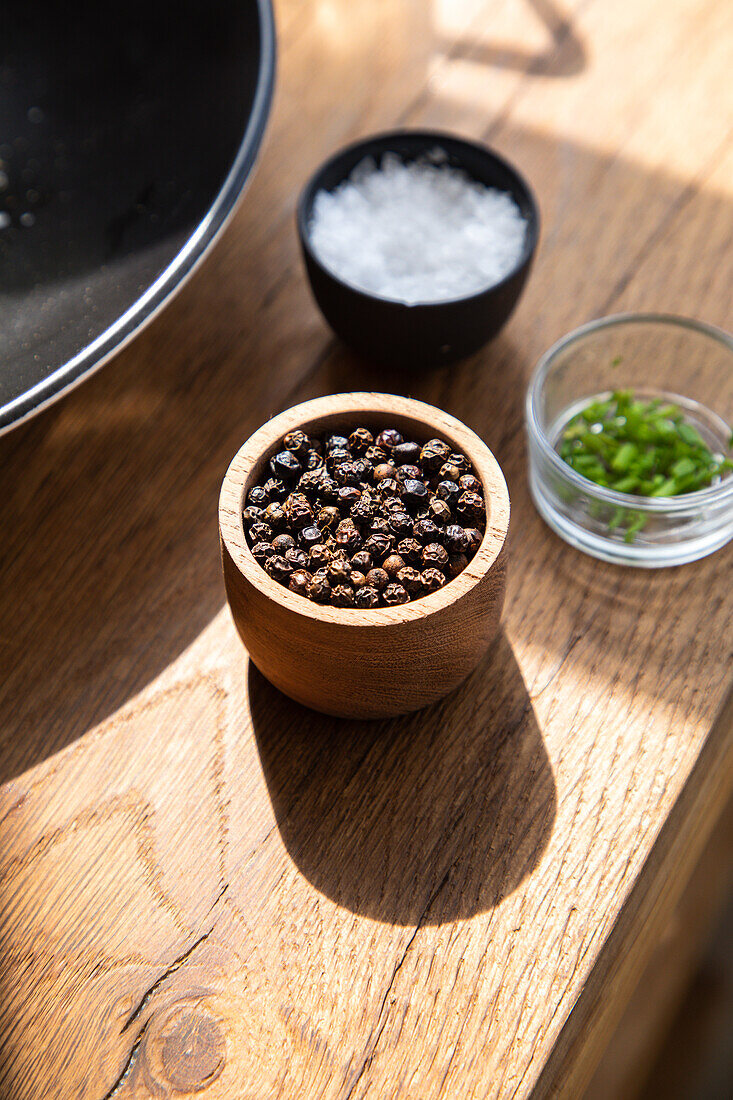 From above of bowl full of spices placed on wooden table near salt in kitchen with bright sunlight at home