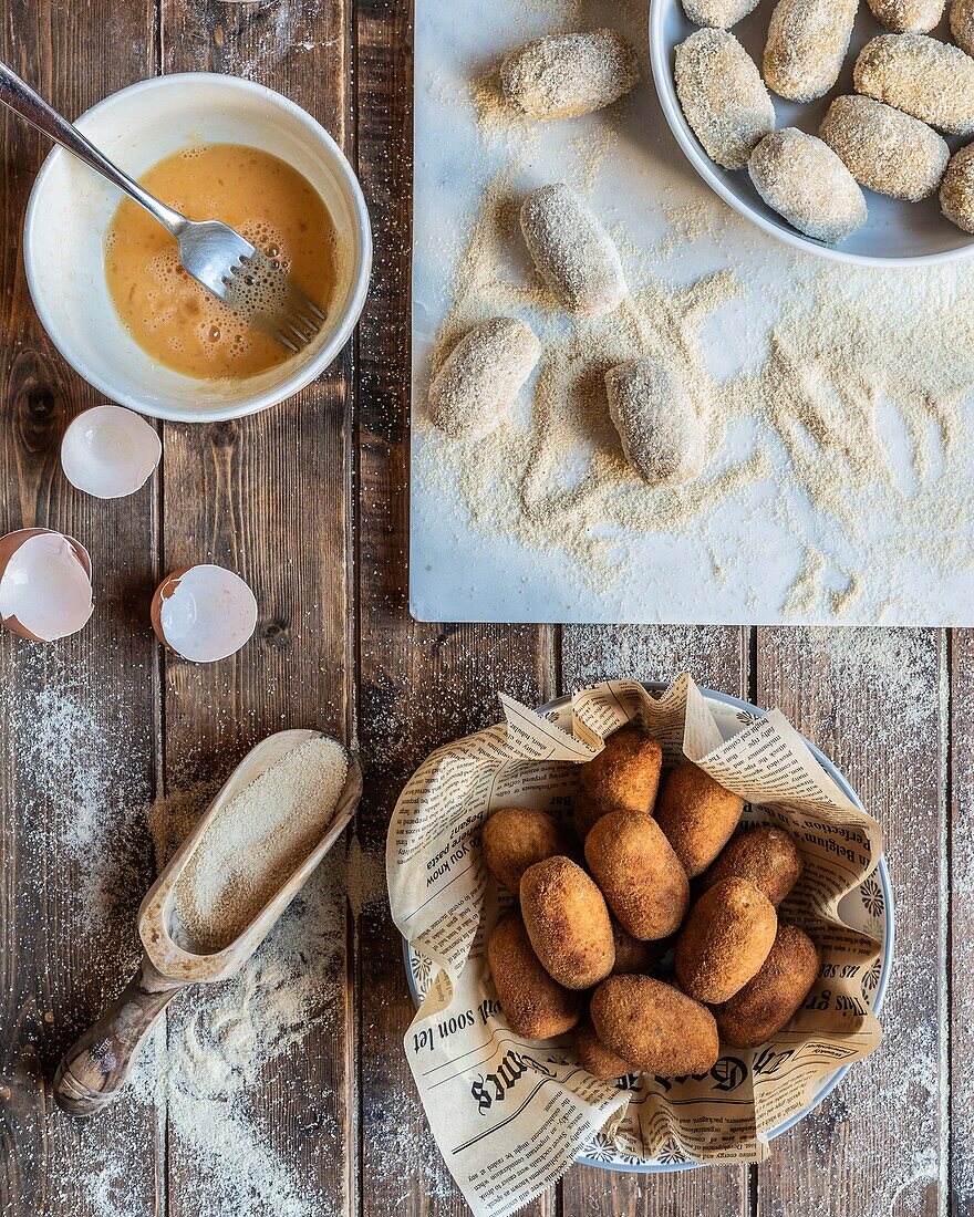 Top view of cooked croquettes in bowl near raw ingredients placed on wooden table during cooking process