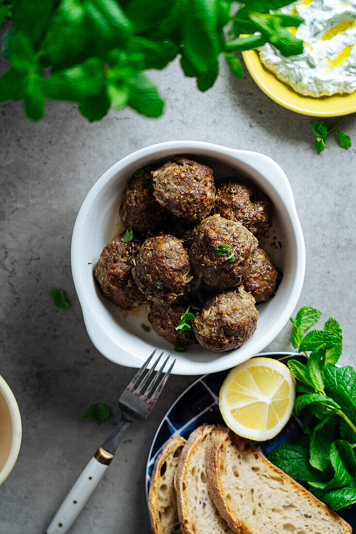 Top view of appetizing traditional homemade fried Greek meatballs served on gray background near plate with bread and lemon in kitchen